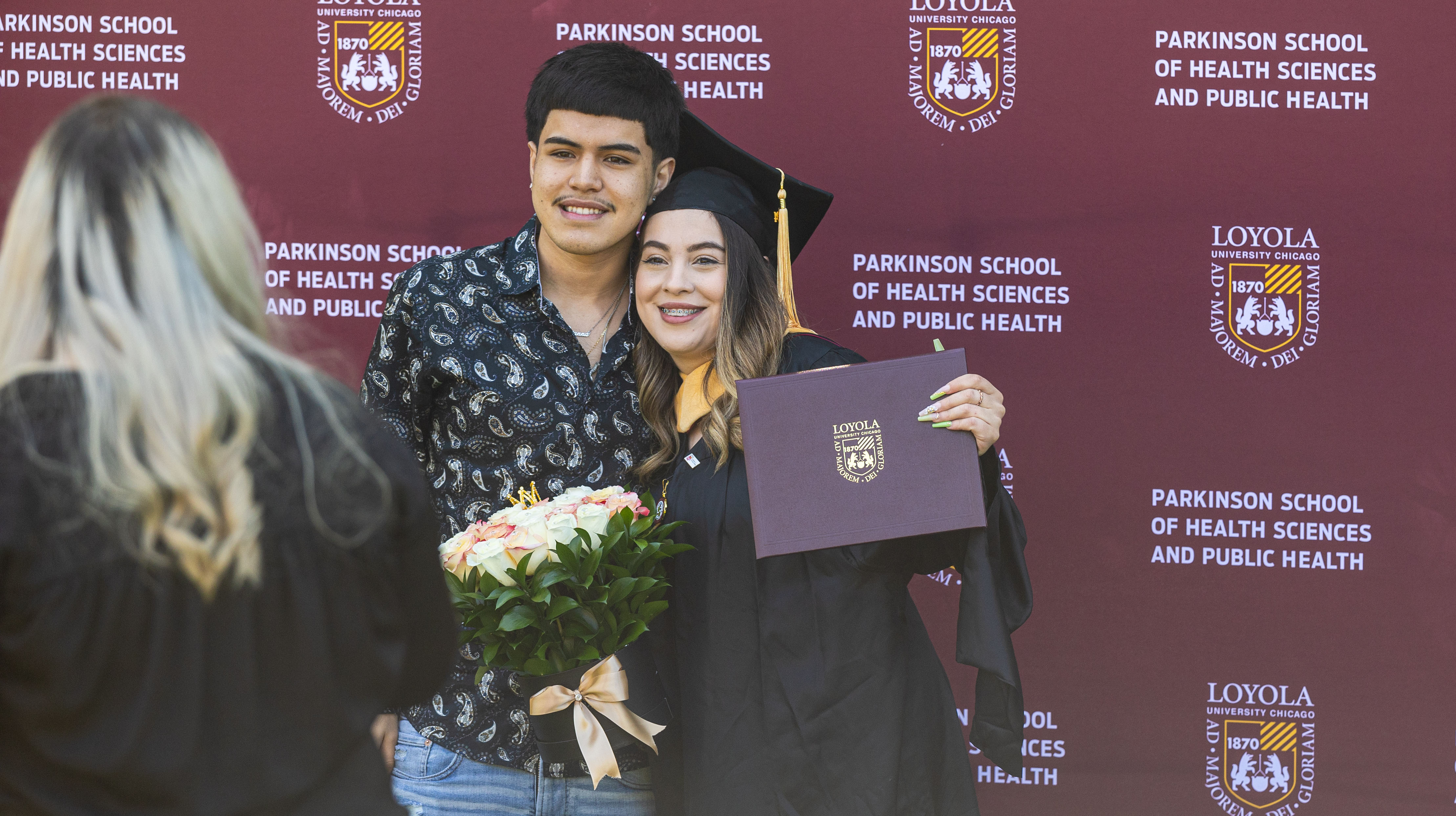 Photo of a graduate and one other person in front of Parkinson backdrop.